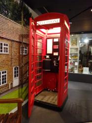 A red telephone box with it's door open, in a room with panels showing photos of the countryside