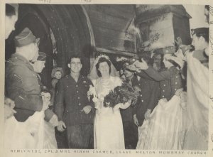 A black and white photograph of a bride and groom exiting a church, surrounded by people celebrating their marriage.