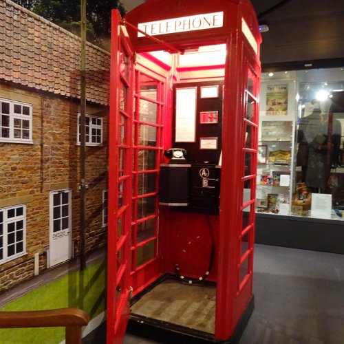 A red telephone kiosk with it's door open, inside a room with panels showing photographs of the countryside on the walls